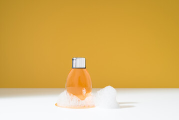 Botella de gel de ducha sobre espuma. Jabón de baño para el cuidado de la piel sobre fondo naranja