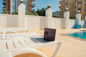 The laptop stands on a sun lounger by the pool