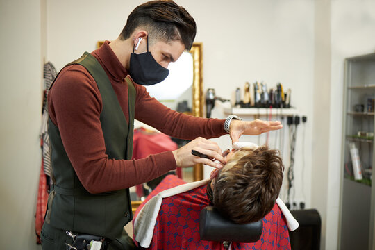 Focused barber trimming beard of male client