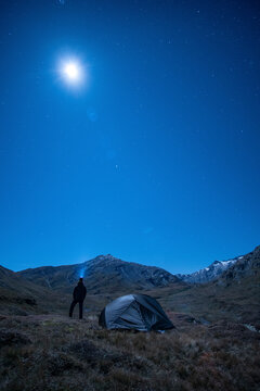 Hiker shining headlamp into moonlit sky in Greina Plains, Grisons, Switzerland