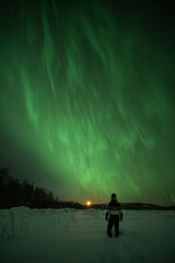 Man looking at moon setting under northern lights in Norrbotten, Sweden