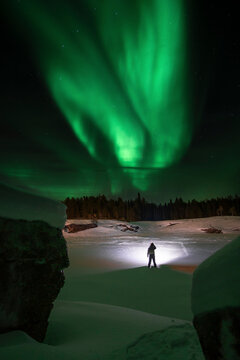 Man on frozen Torne river looking at northern lights in Norrbotten, Sweden