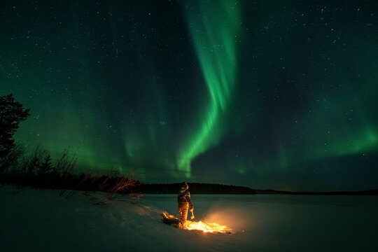 Woman standing next to fire under northern lights in Norrbotten, Sweden 2