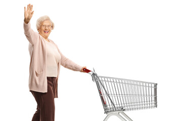 Elderly woman waving and pushing an empty shopping cart