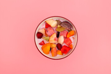 Fruit cocktail with yogurt and shaved ice in bowl, top view. Es Campur or Es Buah on pink...