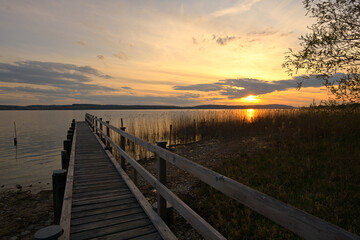 Abendrot an einem See, in den ein Bootssteg aus Holz führt.