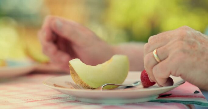 CU Hands of senior man eating melon and strawberry in garden / East Sussex, UK