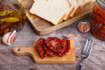 Sun-dried tomatoes in olive oil on a mini board with homemade bread in a rustic style. Traditional home cooking. Selective focus, close-up.