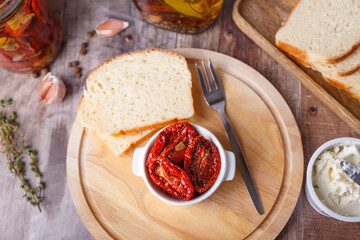 Sun-dried tomatoes in olive oil on a round board with homemade bread and cottage cheese in a rustic style. Traditional home cooking. Selective focus, close-up.