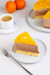 Chocolate-orange mousse cake with biscuit base, jelly and orange circles. Piece of homemade cheesecake and a cup of coffee. Traditional holiday dessert. Selective focus, close-up.