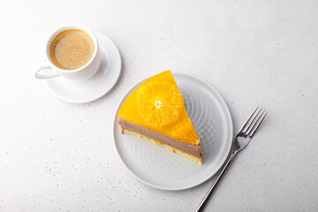 Chocolate-orange mousse cake with biscuit base, jelly and orange circles. Piece of homemade cheesecake and a cup of coffee. Traditional holiday dessert. Selective focus, close-up.