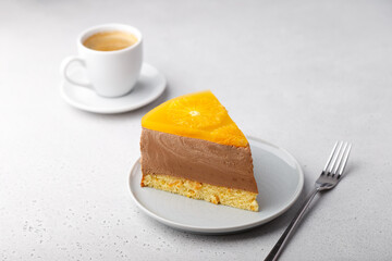 Chocolate-orange mousse cake with biscuit base, jelly and orange circles. Piece of homemade cheesecake and a cup of coffee. Traditional holiday dessert. Selective focus, close-up.