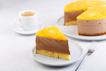Chocolate-orange mousse cake with biscuit base, jelly and orange circles. Piece of homemade cheesecake and a cup of coffee. Traditional holiday dessert. Selective focus, close-up.