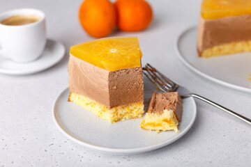 Chocolate-orange mousse cake with biscuit base, jelly and orange circles. Piece of homemade cheesecake and a cup of coffee. Traditional holiday dessert. Selective focus, close-up.