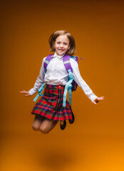 schoolgirl jumping high, rejoicing at the return, school clothes, casual plaid skirt,isolated yellow background