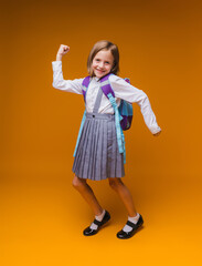 Back to school. A schoolgirl holds books in her hands. a little girl on an isolated yellow studio background. Run and jump, jumping baby. back to school