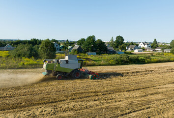 Obraz premium Wheat harvesting. Combine harvester on wheat harvest. Grain and corn markets in crisis world’s breadbasket. Wheat import, maize (corn), soybeans. Rural landscape. Country Houses in countryside.