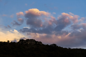 large colored clouds against a background of blue sky and dark silhouettes of mountains and hills. Gradient color.