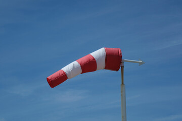 Red-white windsock against the blue sky in sunny weather. Wind vane indicates the strength and direction of the wind