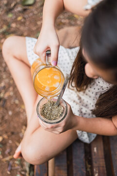 Crop girl pouring lemonade into mate on bench in daytime