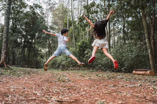 Unrecognizable excited siblings jumping above land in summer