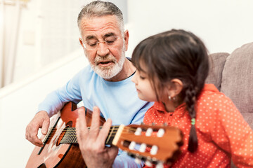 Grandfather teaching kid to play guitar at home