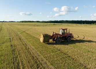 Hay Making in autumn season. Farmer loading round bales of straw from Hay Trailer with a front end...