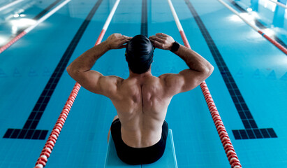 Unrecognizable muscular sportsman siting on block against pool
