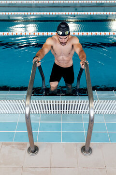 Muscular swimmer in goggles on stairs in pool