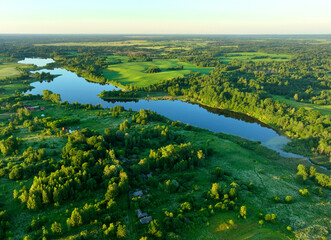 Village at lake, aerial view. Country houses at river in countryside. Roofs of country wooden houses near a pond in village. Green farm fields and forests in rural landscape. Farmland, Agriculture.