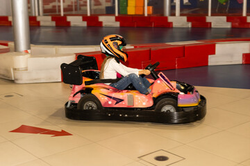 Obraz premium A Little Girl Rides A Car In An Amusement Park. A cute little girl is enjoying a ride on her car. The concept of a happy childhood. Children's leisure. Entertainment for children.