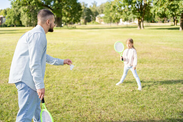 Father and daughter play badminton in park.