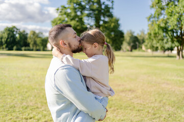 Fototapeta premium stylish bearded father with his little daughter in his arms on a walk in the summer park hugging and kissing