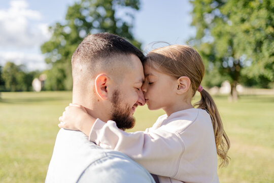 Daughter hugging and kissing her father in the park, father and daughter outdoors smiling face to face