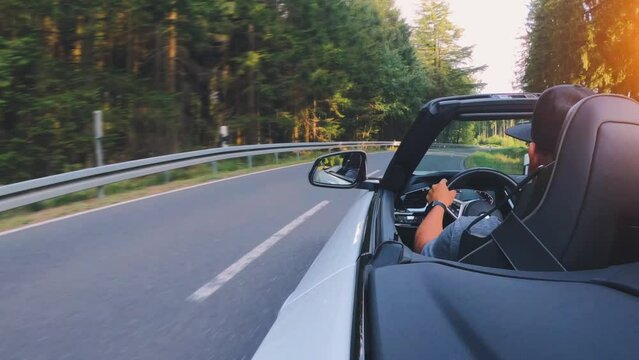 Adult man is driving with convertable car in sunny nature on a bright summer day. wide angle pursuit shot