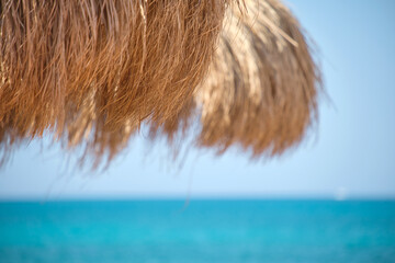 Straw shade umbrella in sea tropical region against blue vibrant sky in summer