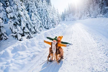 Fotobehang Happy funny children ride wooden retro sleds on snowy road in mountains. Family on winter walk. © Olha