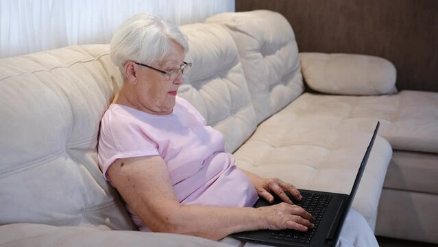 Happy Elderly Woman Using Laptop Computer At Home. Senior Mature Older Woman Watching Business Training, Online Webinar On Laptop Computer Remote Working Or Social Distance Learning From Home. 60s Bus