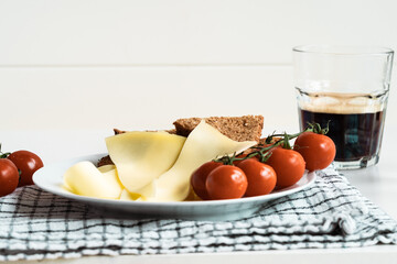 Breakfast plate with gouda cheese, bread, tomatoes and glass of fresh coffee