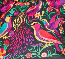 Fototapeta na wymiar Handmade colorful fabric from Chiapas, Mexico. Birds and flowers edged in various colors on a black background.