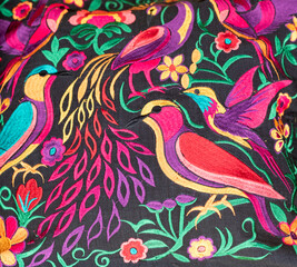 Handmade colorful fabric from Chiapas, Mexico. Birds and flowers edged in various colors on a black background.