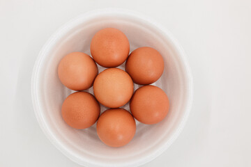 Seven raw chicken eggs in a styrofoam cup with white background.