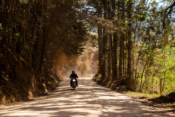 Motociclista com farol ligado levantando poeira na estrada