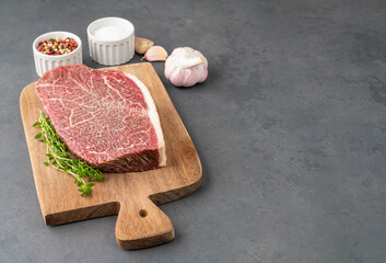 Raw wagyu shoulder roast meat over wooden board with seasonings and copy space