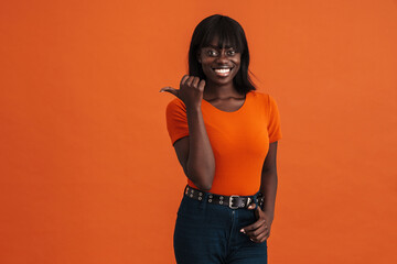 Image of smiling african woman pointing aside over orange background
