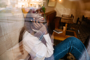 View through window on young smiling african woman talking phone