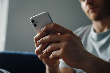 Young bearded man using cellphone while sitting on sofa at home
