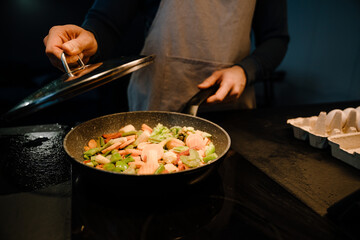 Young white man wearing apron cooking dinner with frying pan at home