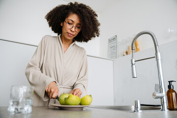 African american young woman cutting apples at kitchen in morning