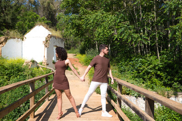 Fototapeta na wymiar Young and handsome latin dance couple salsa and bachata in the park on a wooden bridge. The couple dances passionately and in love surrounded by greenery and trees. Dance concept.
